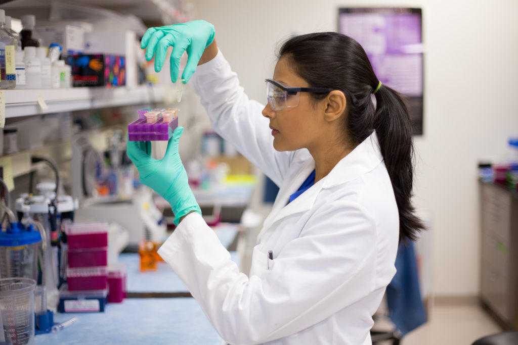 Person in a lab coat and teal gloves looking at test samples