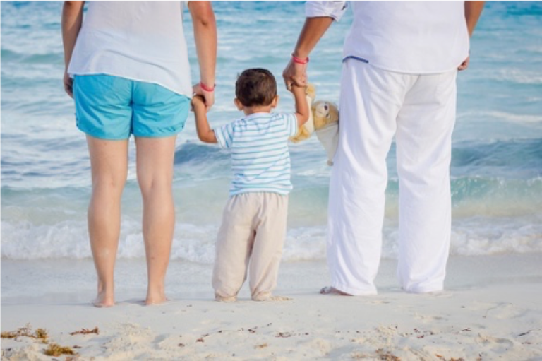 Two adults standing on the beach holding hands with a child that is between them